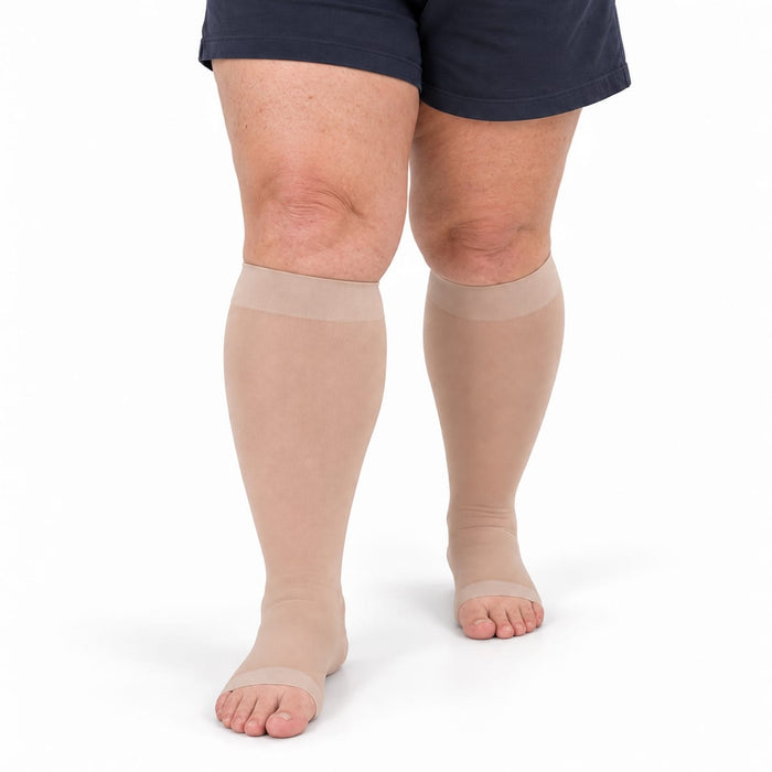 Henkilöllä on jalassaan Kroppsbutikin avokärkiset kompressiosukat, 20–30 mmHg, plus-kokoa, valkoisella pohjalla.