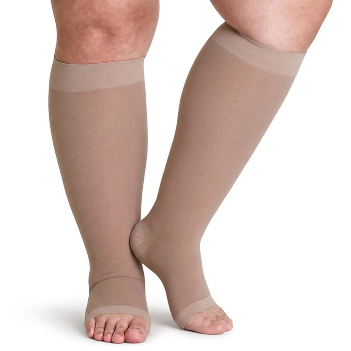 Henkilöllä on polvipituiset, beigeä väriset avovarvaskompressiosukat, paine 20–30 mmHg, Plus Size.